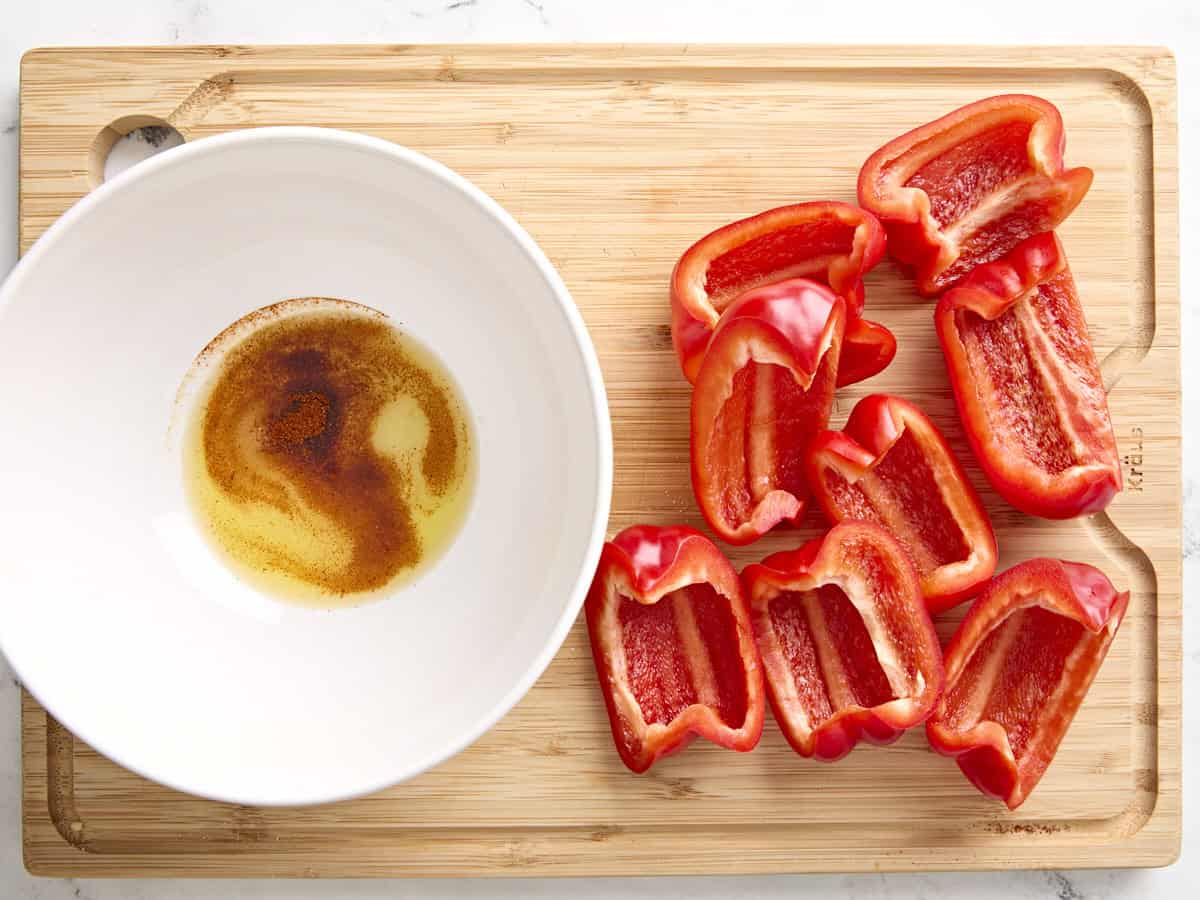 Quartered and seeded red bell peppers next to a bowl of seasoning