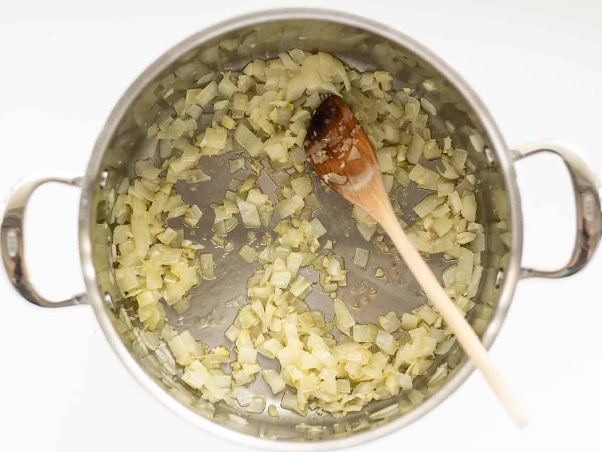 Sautéed onion and garlic in a soup pot with a wooden spoon.