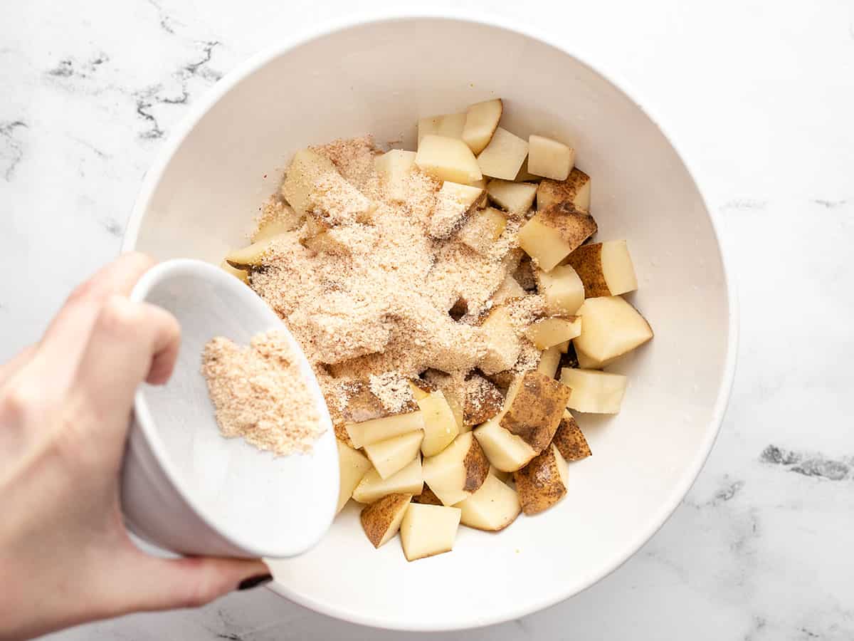 Seasoning being sprinkled over diced potatoes in a bowl. 