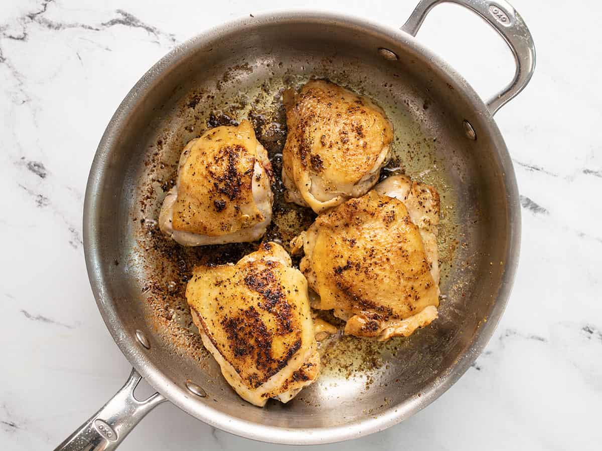 Browned chicken thighs in the skillet.