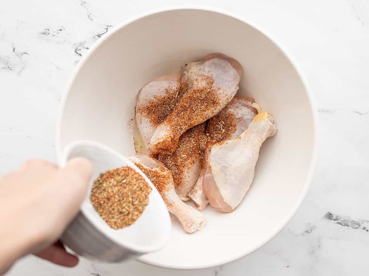 Seasoning being sprinkled over chicken drumsticks