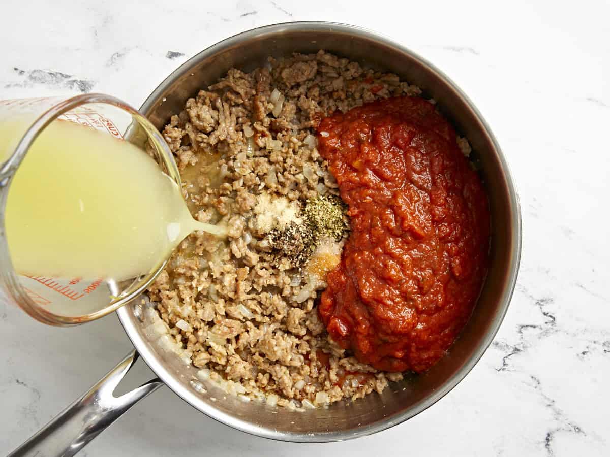 Marinara sauce, spices, and chicken broth added to a skillet.