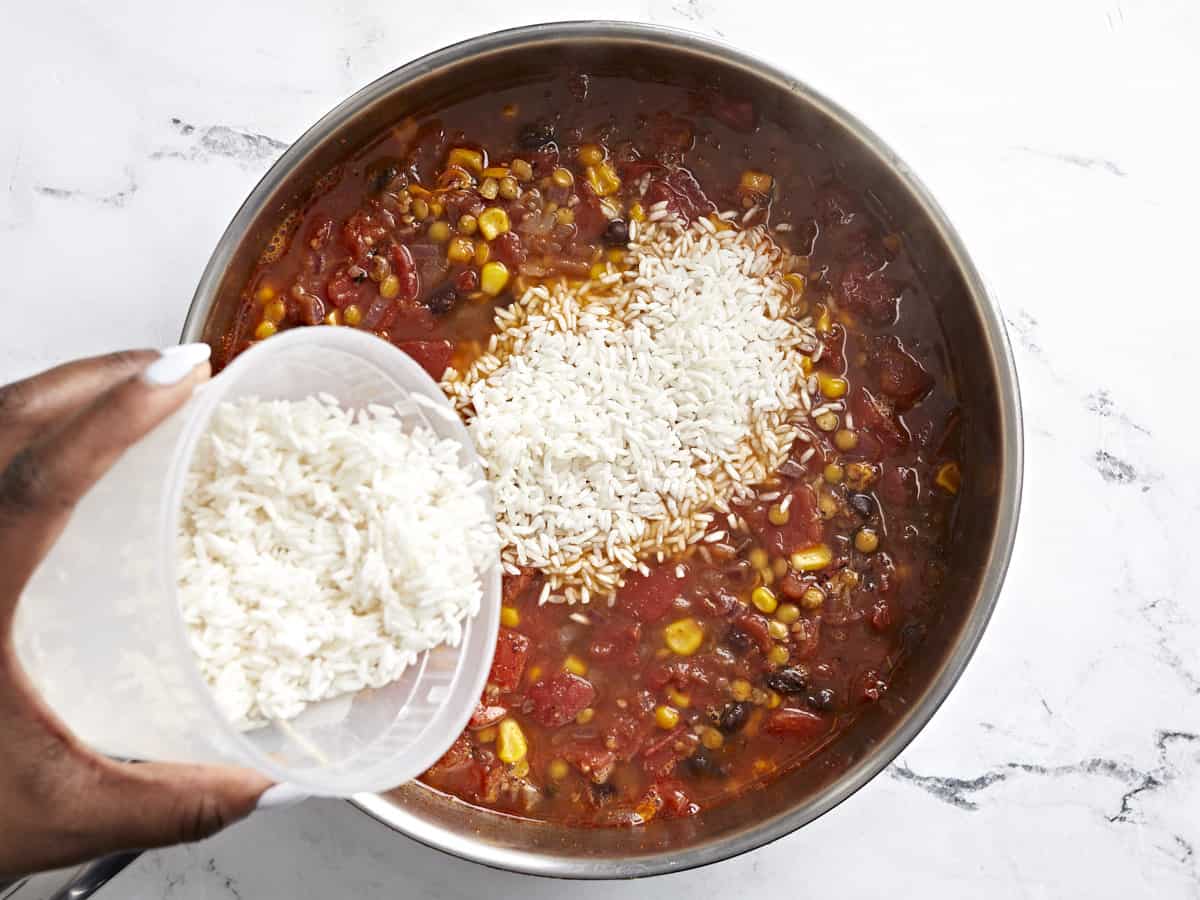 Long grain white rice being added to the skillet.