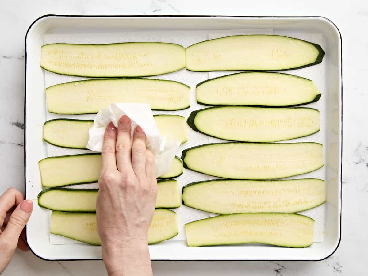 A hand dabbing zucchini slices dry with a paper towel