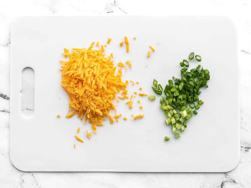 Shredded cheddar and sliced green onion on a cutting board