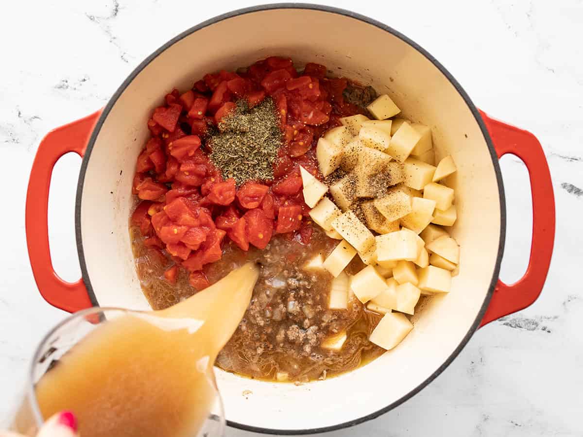 Tomatoes, potatoes, herbs, and broth added to the pot.