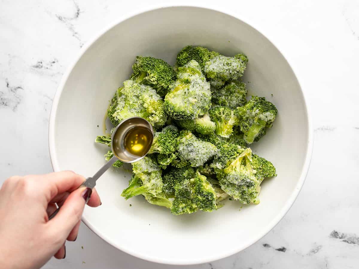 Frozen broccoli in a bowl with oil being drizzled over top.