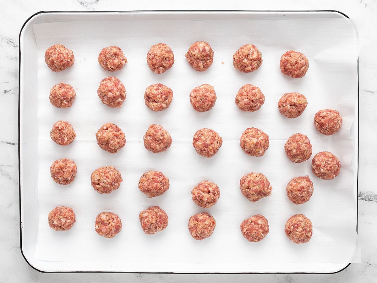 Shaped meatballs on a baking sheet lined with parchment paper. 