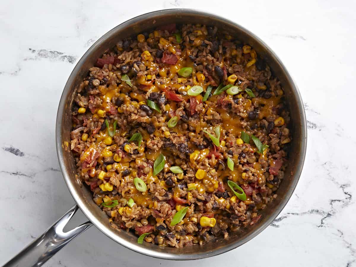 Finished Southwest Lentils and Rice Skillet with shredded cheddar cheese and sliced green onions on top.