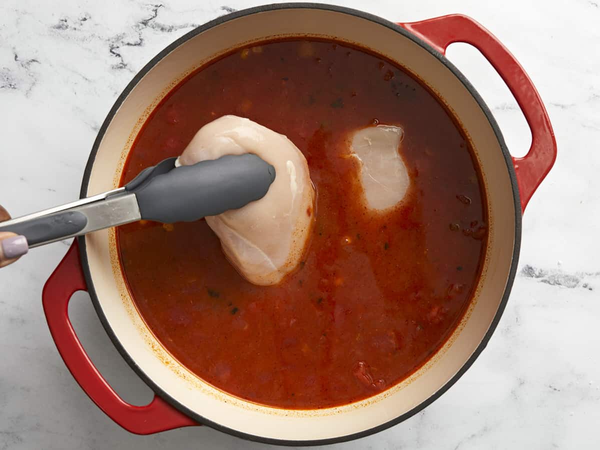 Two chicken breasts being placed in the dutch oven on top of the soup ingredients.