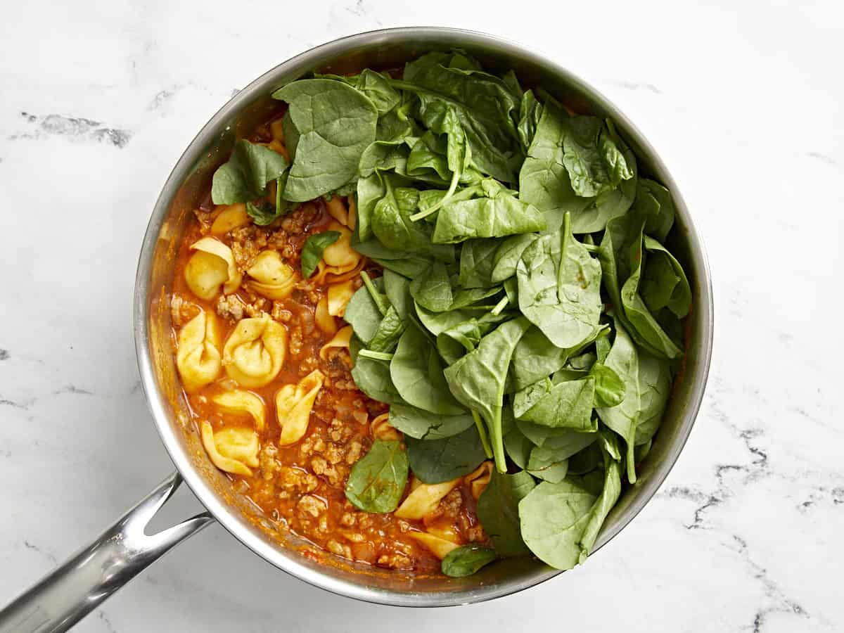 Spinach added to tortellini and sausage mixture in a skillet.