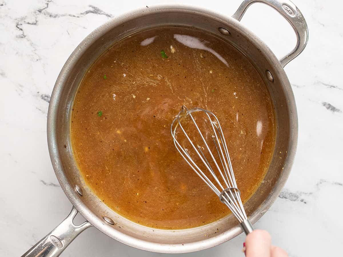 Broth being whisked in the skillet to dissolve chicken drippings.