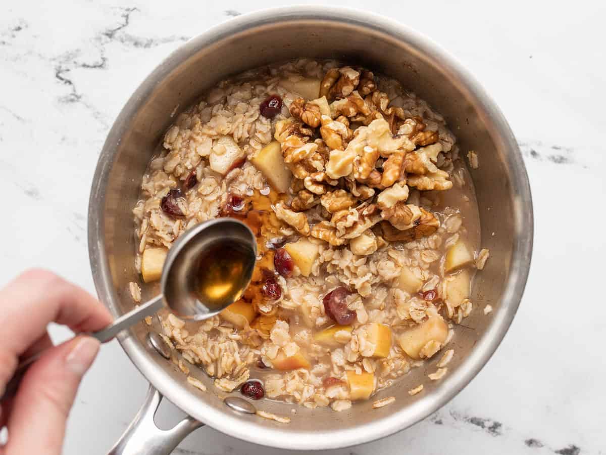 maple syrup being drizzled over the thickened oats in the pot