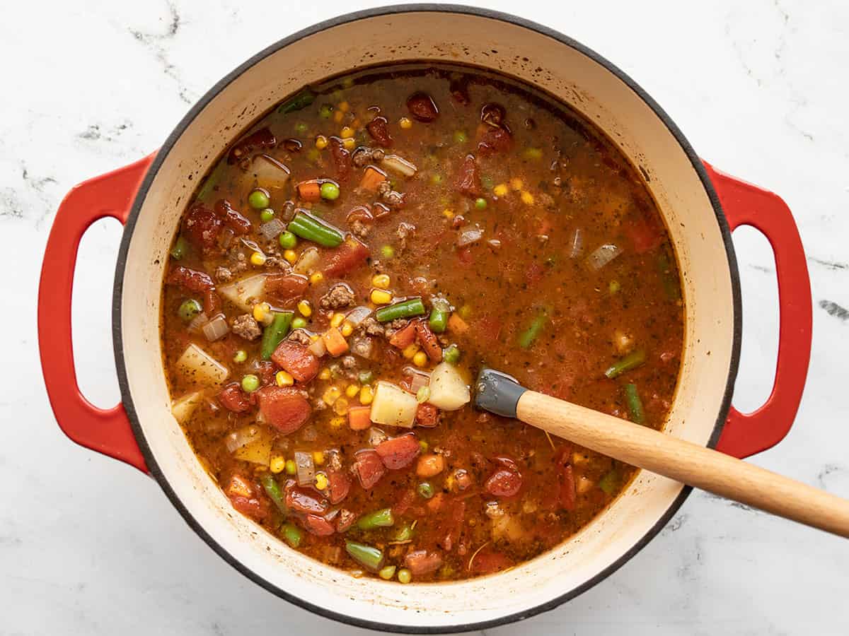 Finished vegetable beef soup in the pot with a spoon.