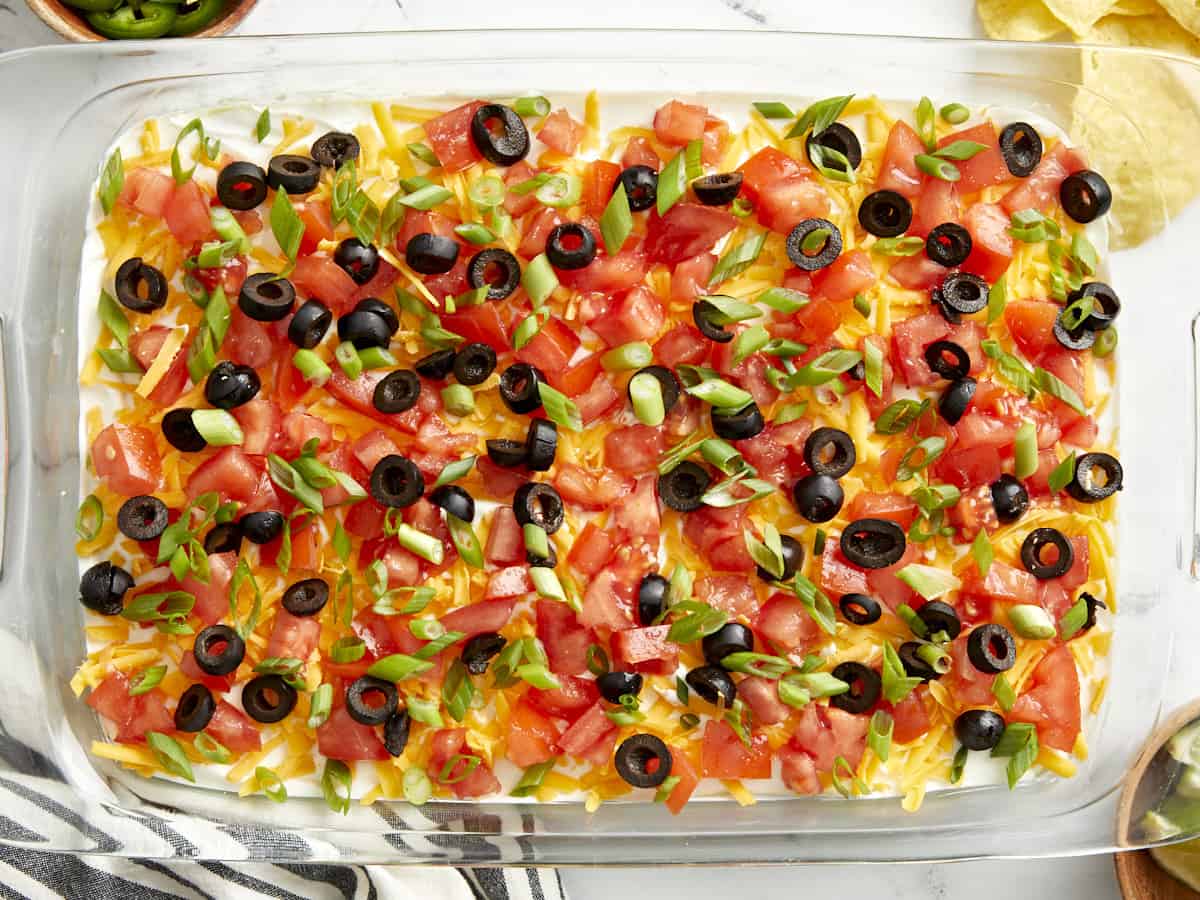 Overhead view of 7 layer dip in a glass casserole dish with a napkin, chips, and lime wedges on the side.