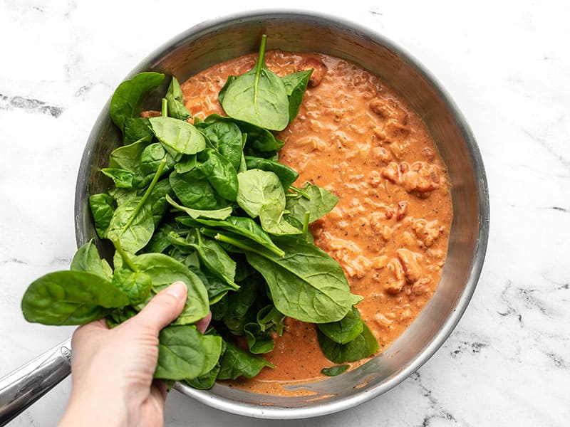 Fresh spinach being added to the skillet