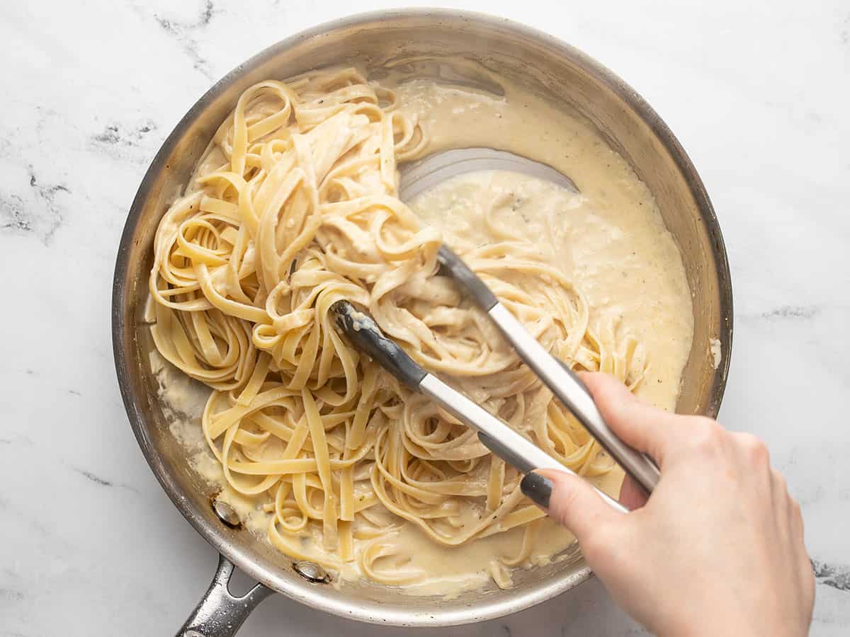 Fettuccine being tossed in the cream sauce.