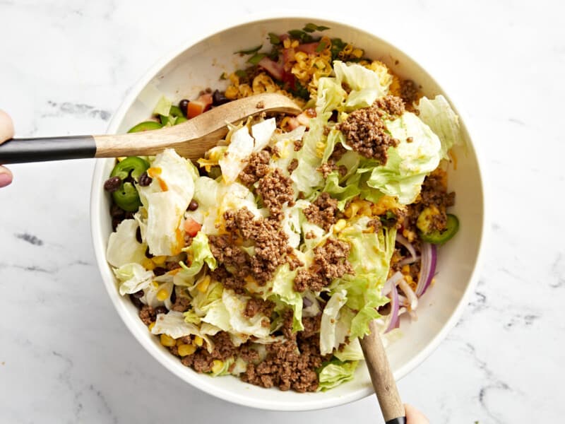 tossing taco salad in a white bowl.