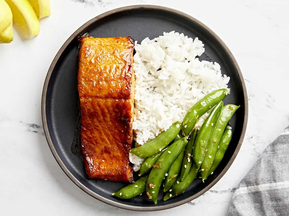 overhead view of a serving of air fryer salmon on a black plate with rice and peas.