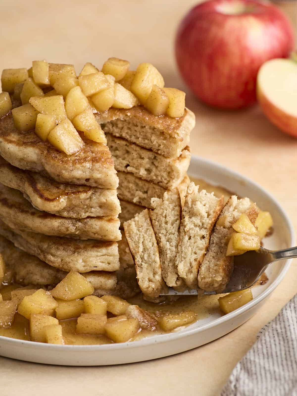 Front view of a stack of apple cinnamon pancakes with fork lifting some out.