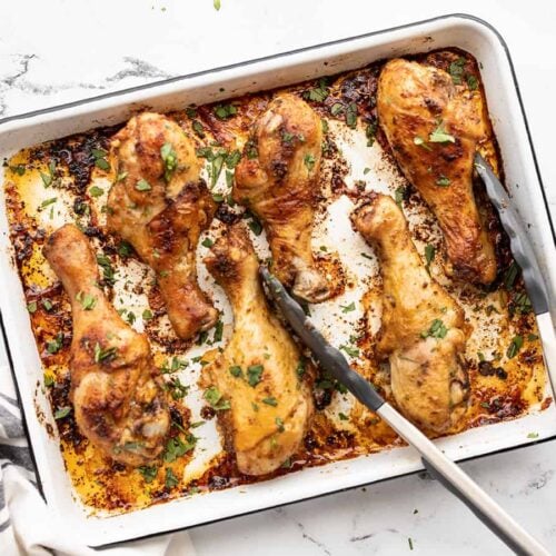 Oven roasted chicken drumsticks on a baking sheet with tongs