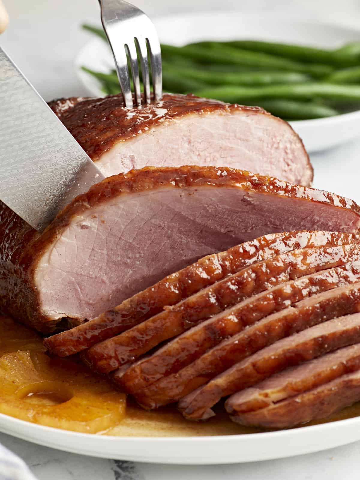 slicing a baked ham on a white plate with pineapple rings.