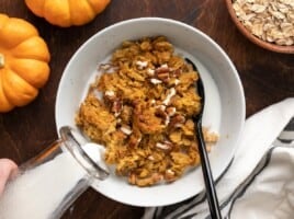 Milk being poured into a bowl of pumpkin pie oatmeal with nuts.