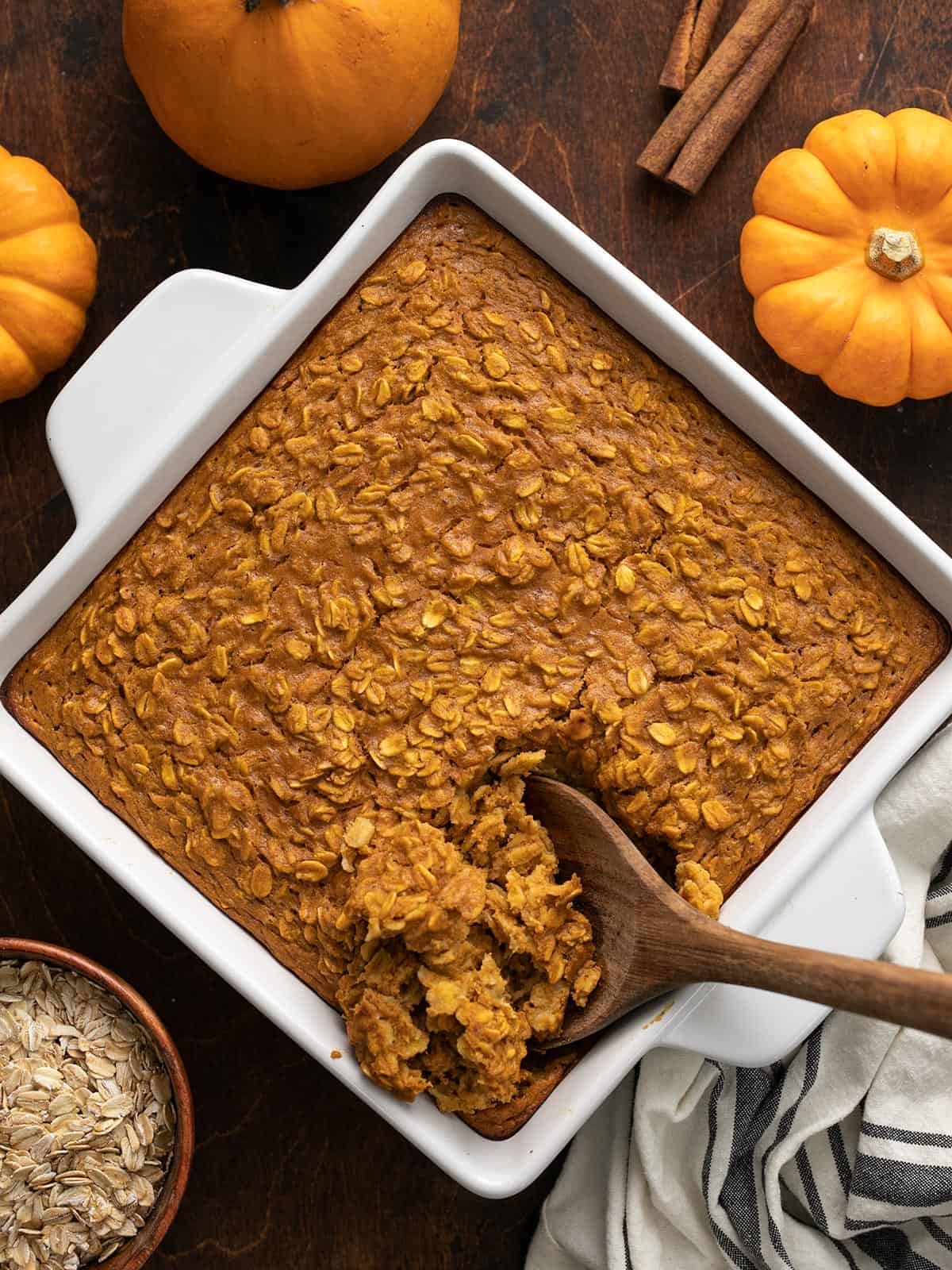 Overhead view of baked pumpkin pie oatmeal in the baking dish being scooped with a wooden spoon.