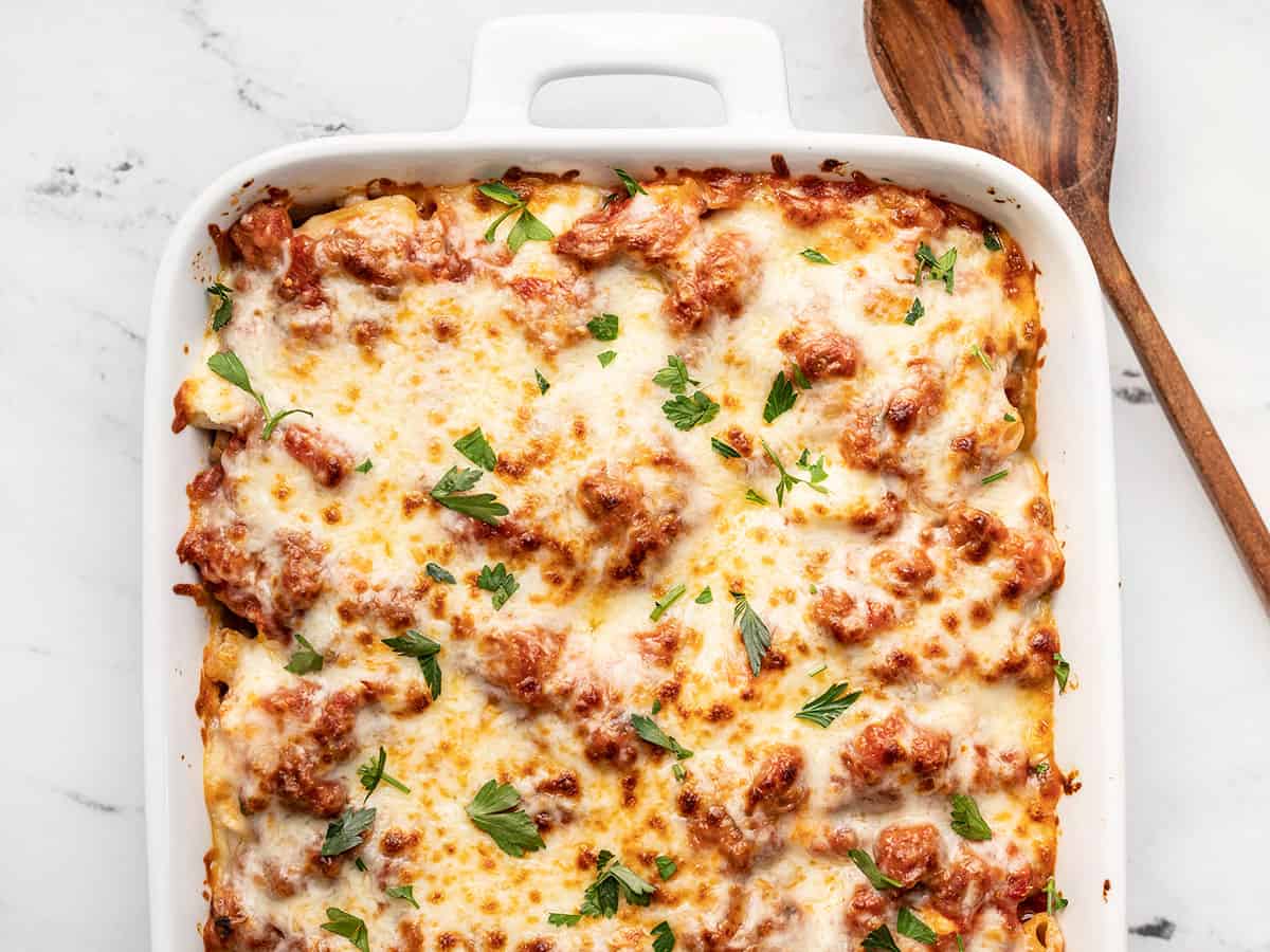 Overhead view of baked ziti in the casserole dish with a wooden spoon on the side.