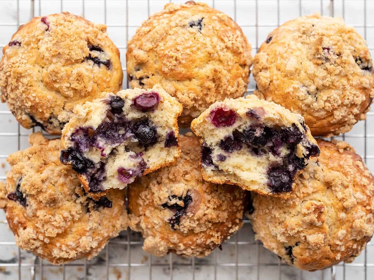 Overhead view of blueberry muffins on a cooling rack with one torn in half. 