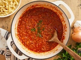 Overhead shot of bolognese in a beige Dutch oven with a wood spoon in it.