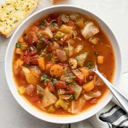 a bowl of cabbage soup with a spoon and garlic bread on the side