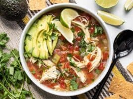 Finished bowl of Chicken and Lime Soup with sliced avocado and a couple of lime wedges