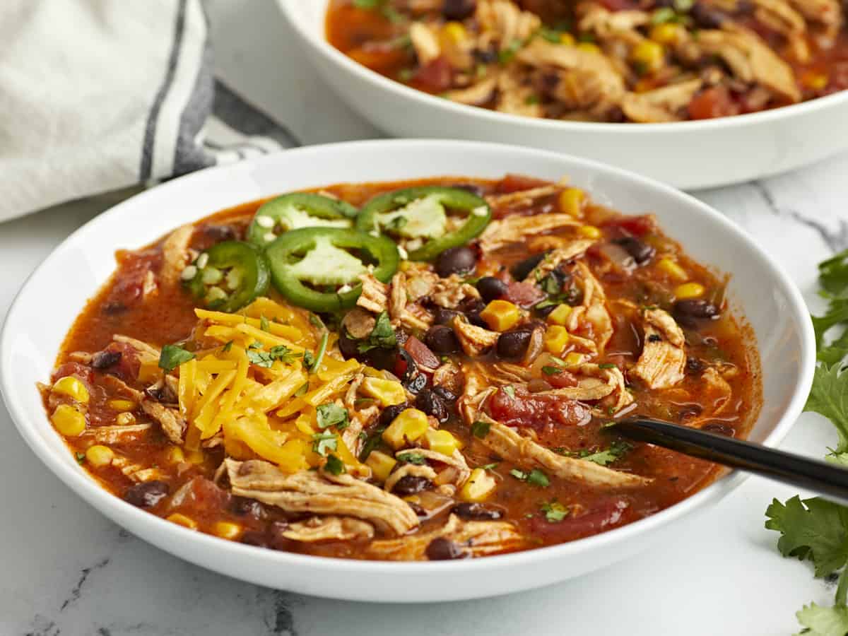 Side view of two bowls of chicken enchilada soup with a black spoon inside the soup.