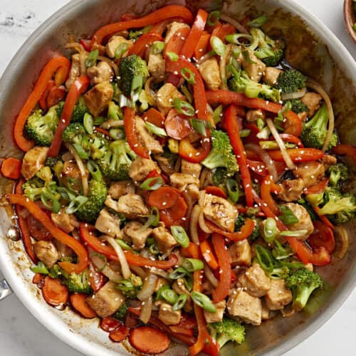 Overhead view of chicken stir fry in a large skillet with sliced green onions on the side.