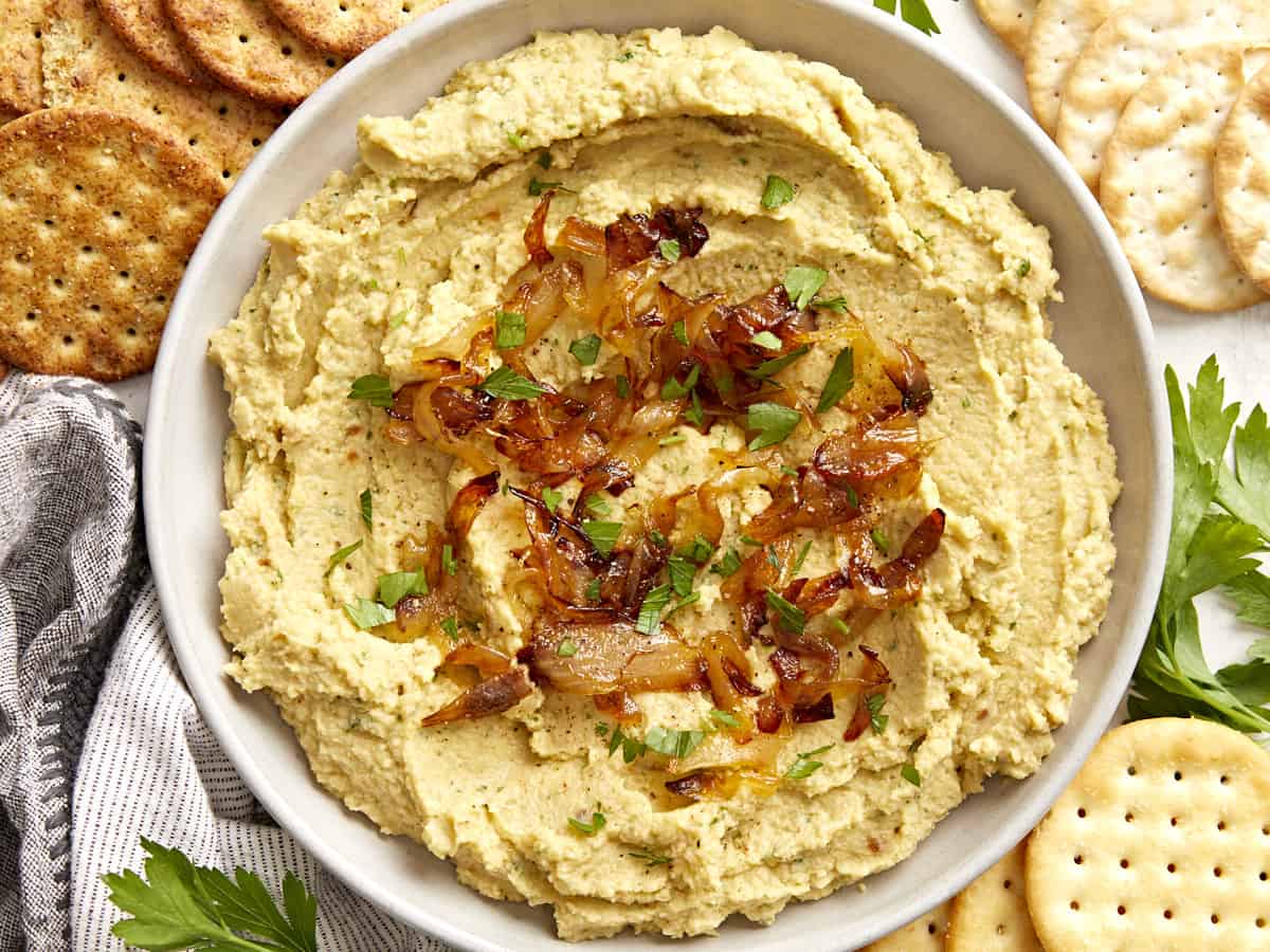 Overhead view of a bowl full of chickpea spread with caramelized onions surrounded by crackers.