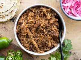 Overhead view of a bowl full of chili rubbed pulled pork with taco fixings on the sides