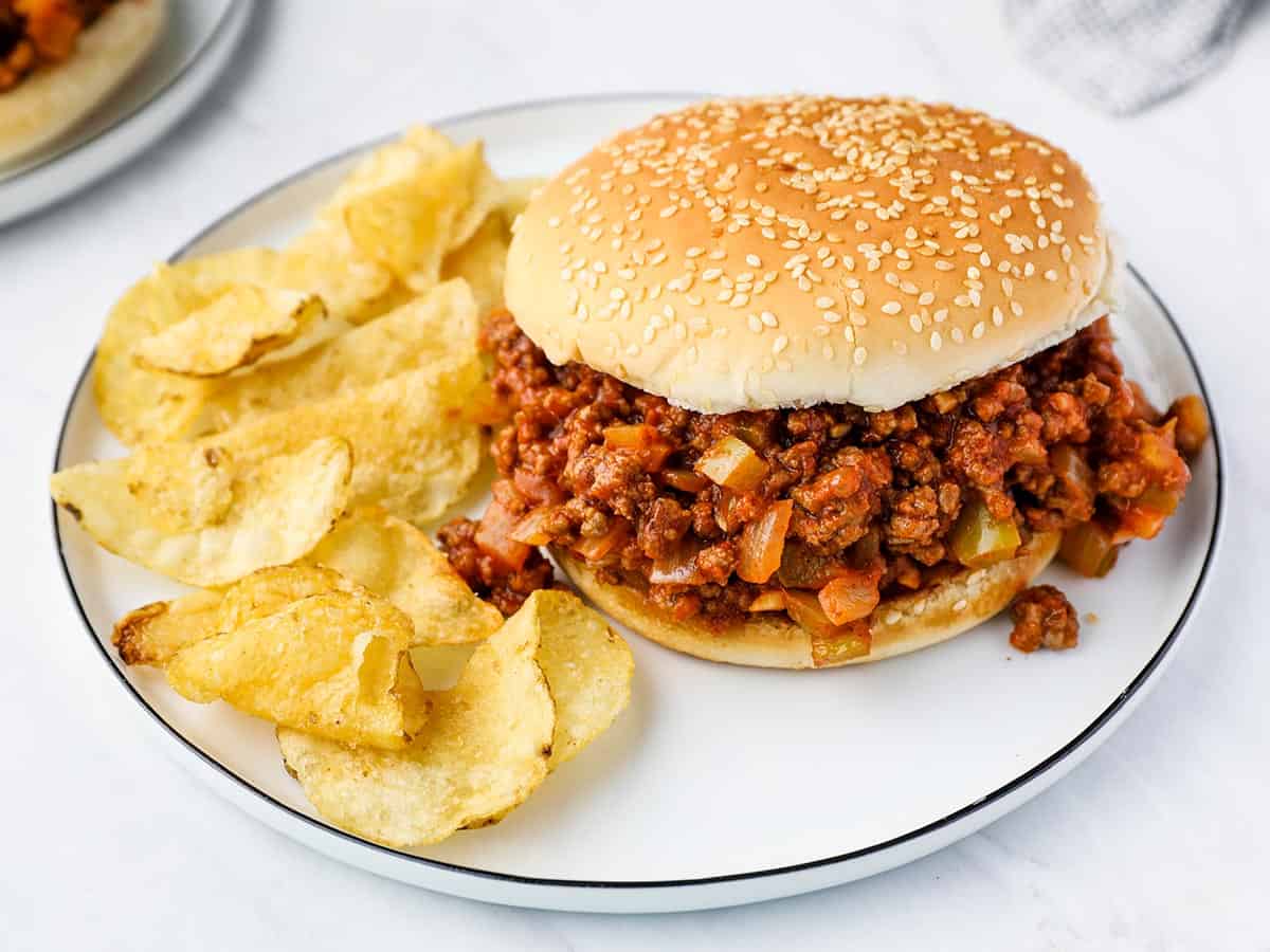 A sloppy joe on a plate with potato chips.