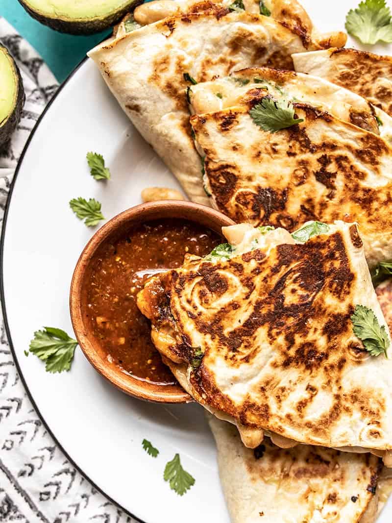 Close up of a quesadilla being dipped into a bowl of red salsa