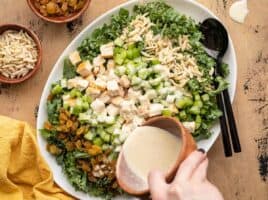 dressing being poured over kale and chicken salad