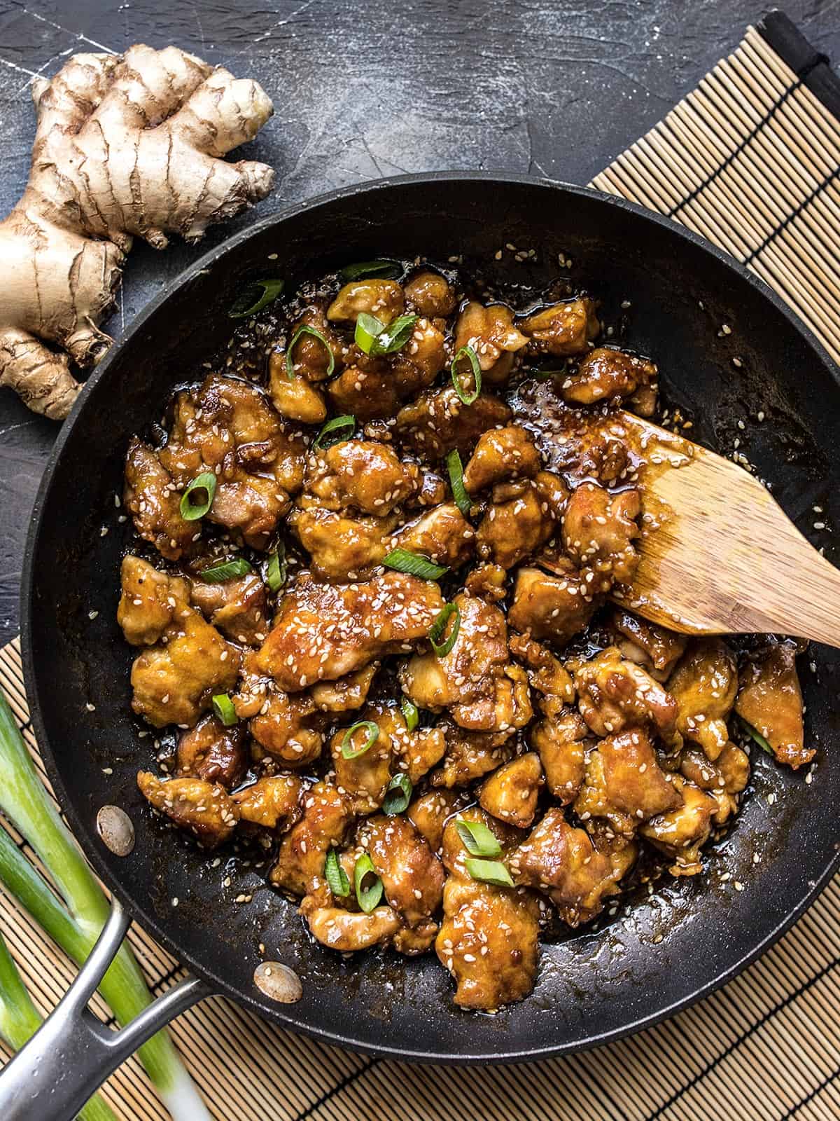 Overhead view of a frying pan full of sesame chicken with a wooden spatula.