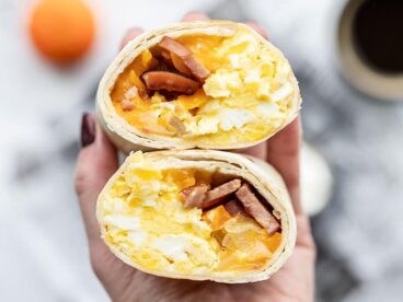 The open sides of a cut open breakfast burrito held toward the camera, close up.