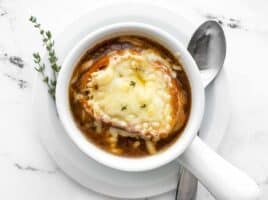 Overhead view of one bowl of french onion soup with a spoon and fresh thyme on the side