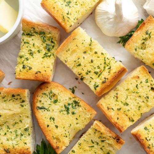 Slices of homemade garlic bread spread out on a surface.