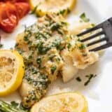 A fork picking at a piece of garlic butter baked cod on a plate