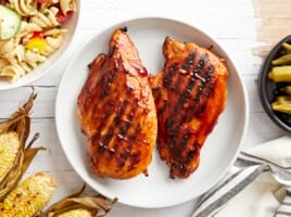 overhead view of 2 grilled bbq chicken breasts on a white plate.