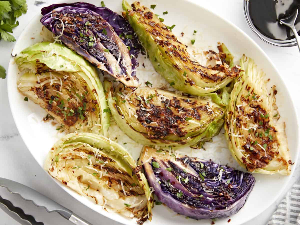 Grilled cabbage wedges on a platter, topped with balsamic glaze, Parmesan cheese, and fresh parsley.