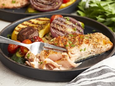 cutting a piece of grilled salmon on a black plate with a fork.