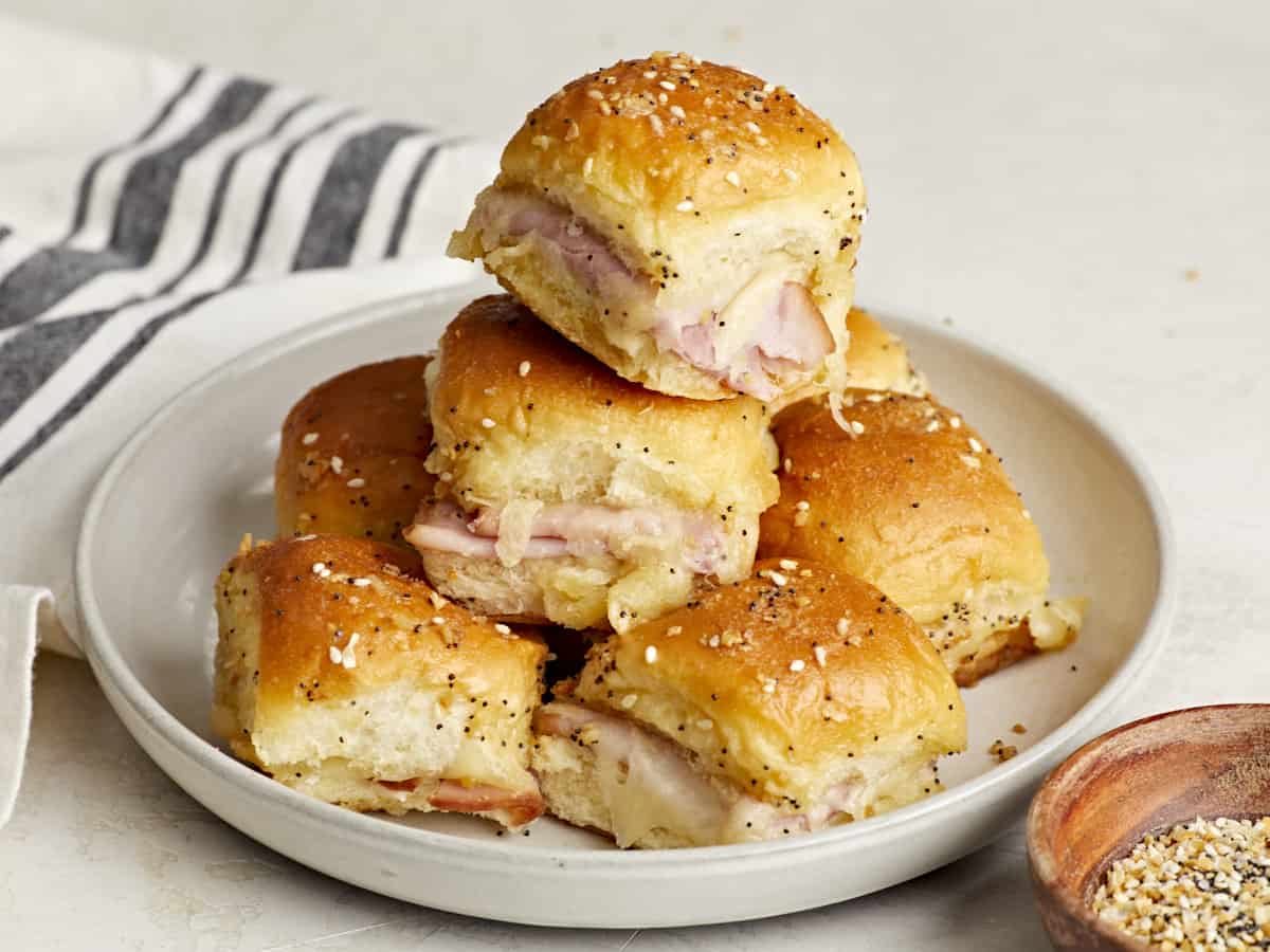 Front side view of a stack of ham and cheese sliders on a plate.