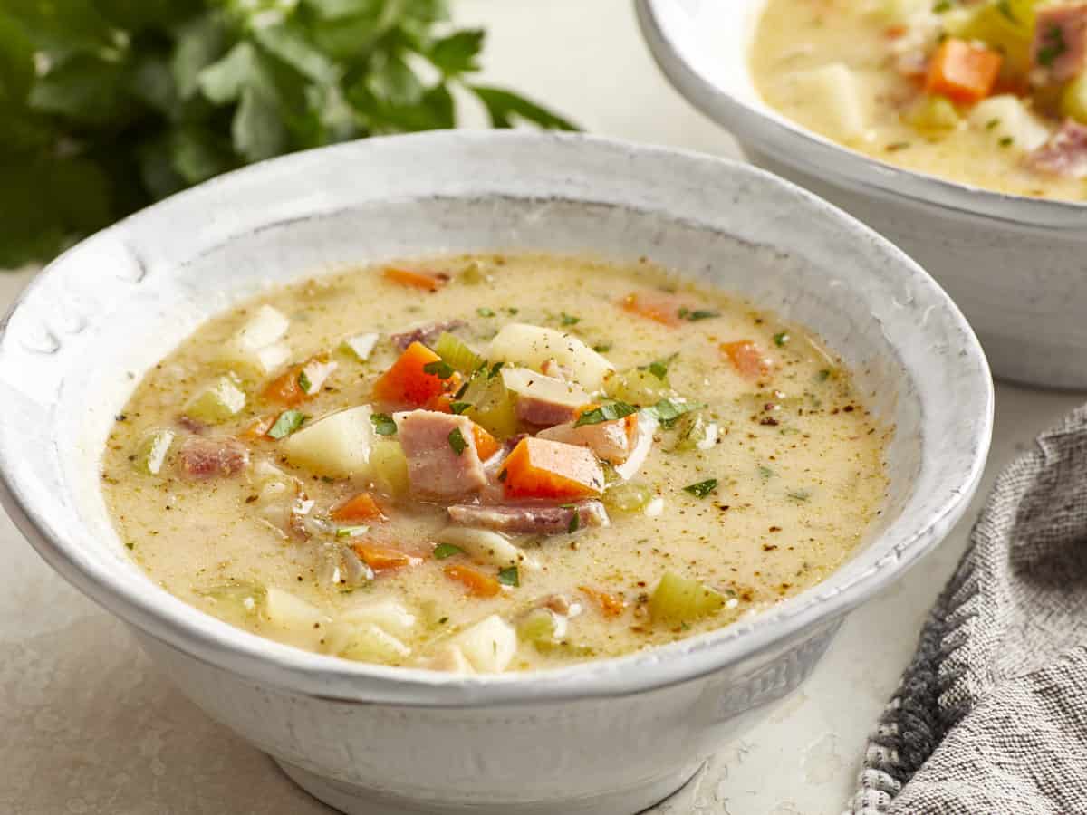 three-quarters view of a serving of ham and potato soup in a white bowl.